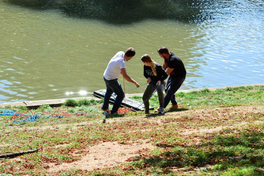 Three people pulling a magnet out of a lake while magnet fishing